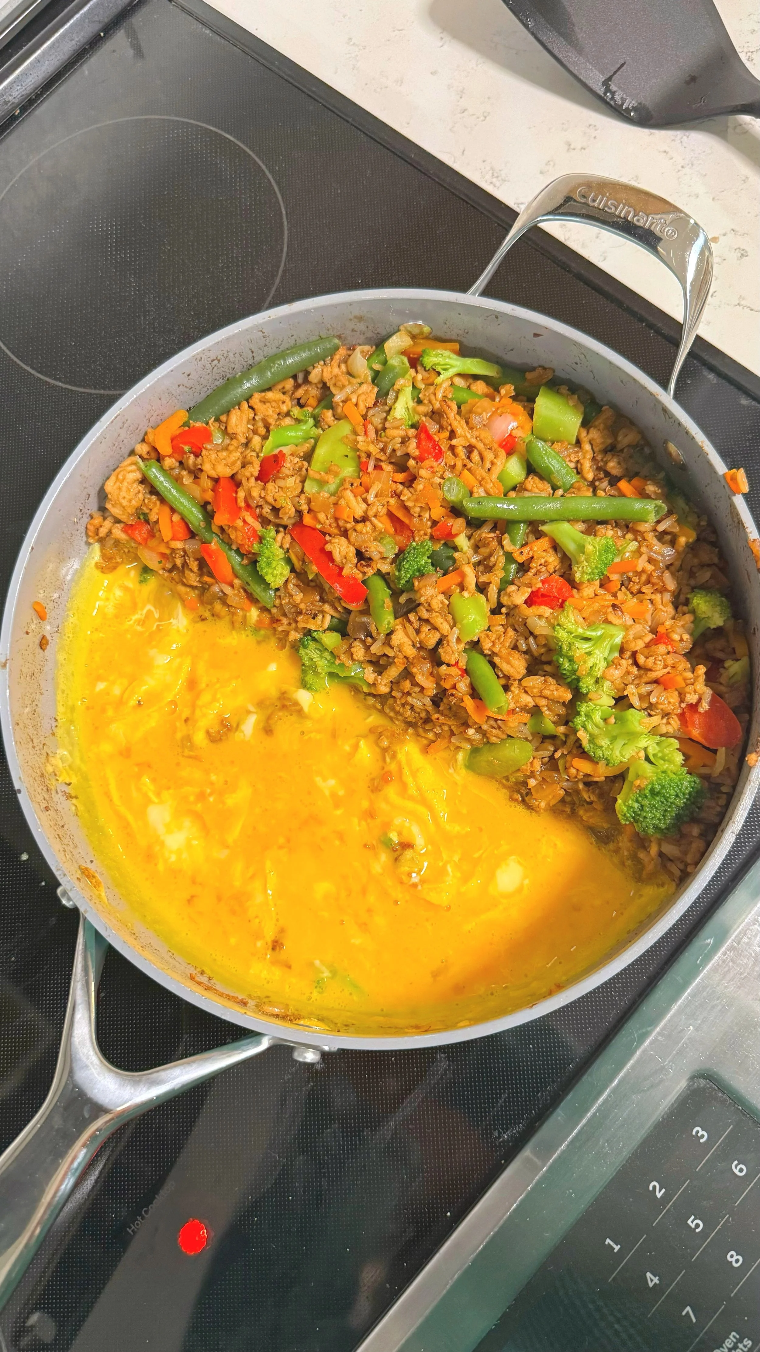 A pan of chicken fried rice with mixed vegetables on one side and eggs cooking on the other side.