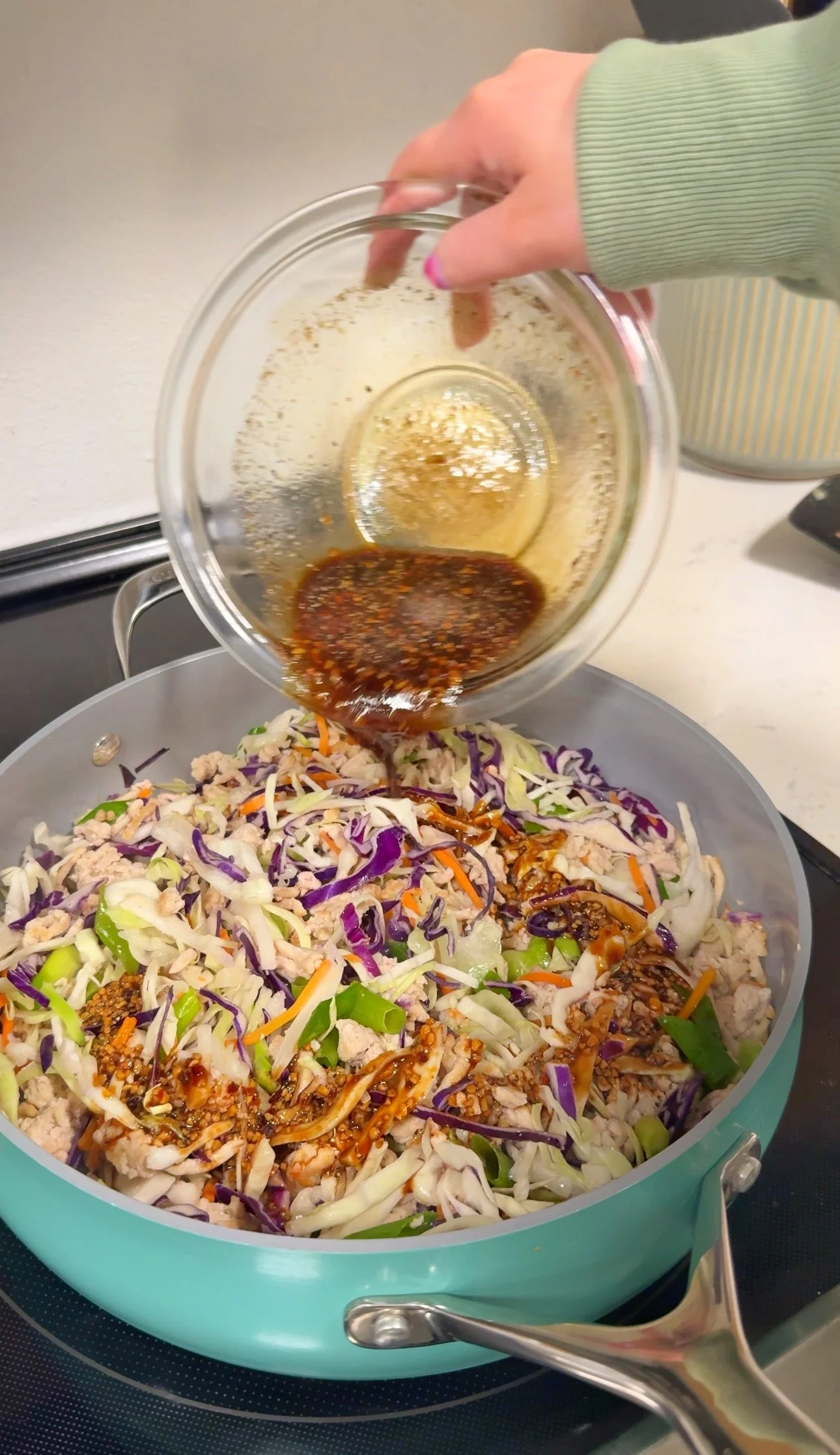 A pan with a cabbage slaw and chopped green onions with a sauce being poured over it.