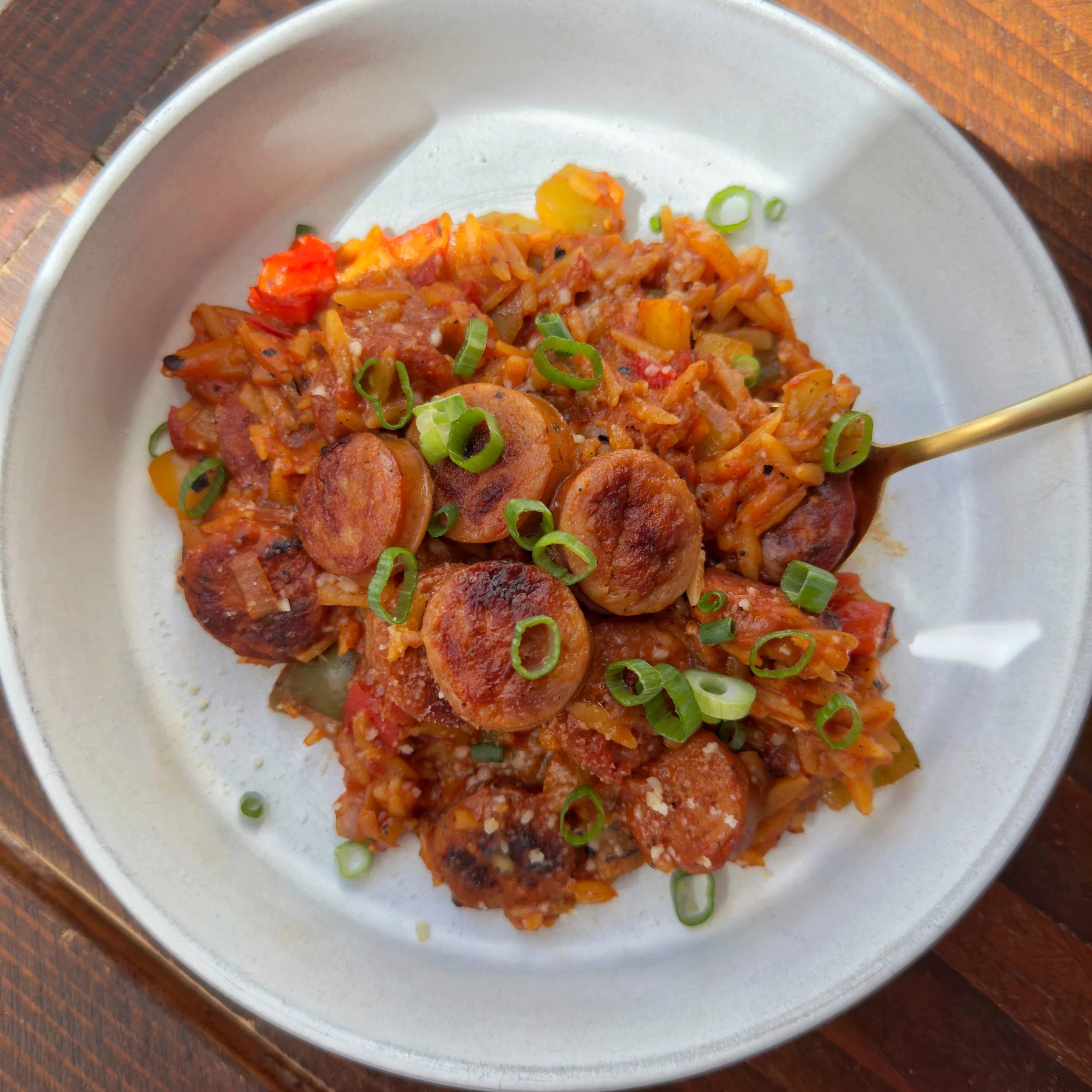A bowl of cajun chicken sausage with bell peppers, fire roasted tomatoes over orzo topped with chopped green onions.