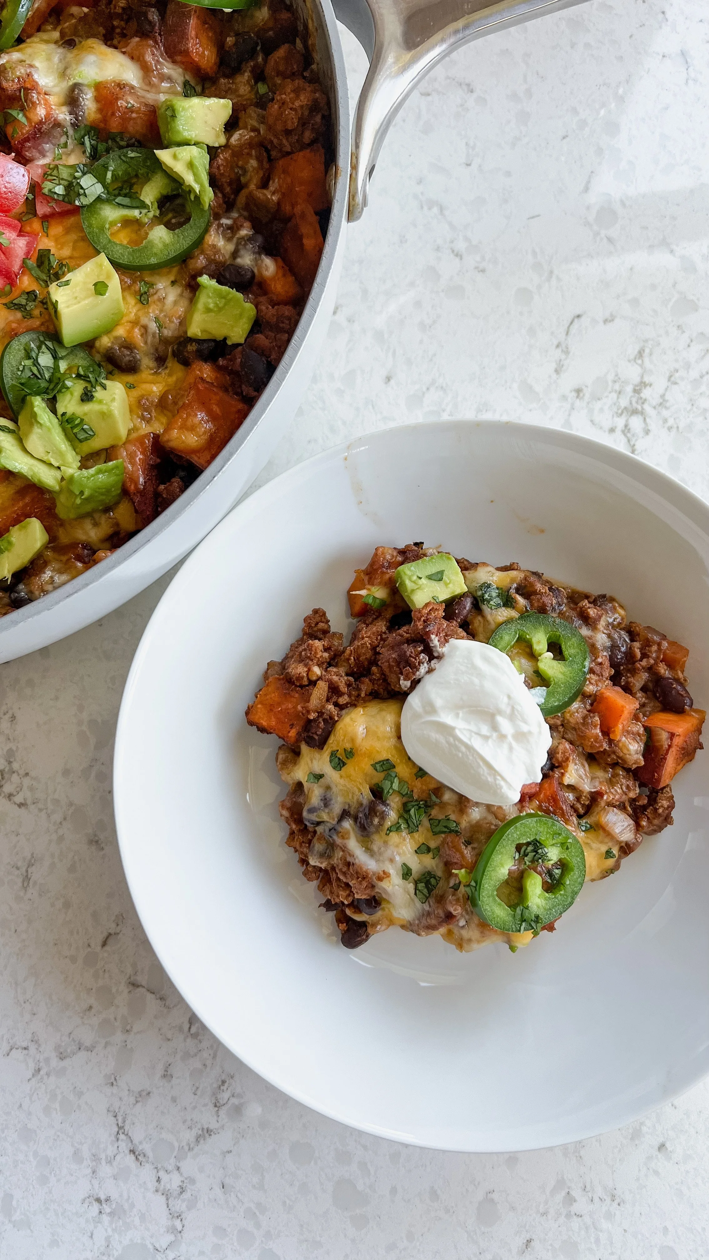 A bowl of ground turkey, sweet potatoes, tomatoes, avocado, Jalapeno's, fresh cilantro with a drop of sour cream on top. 