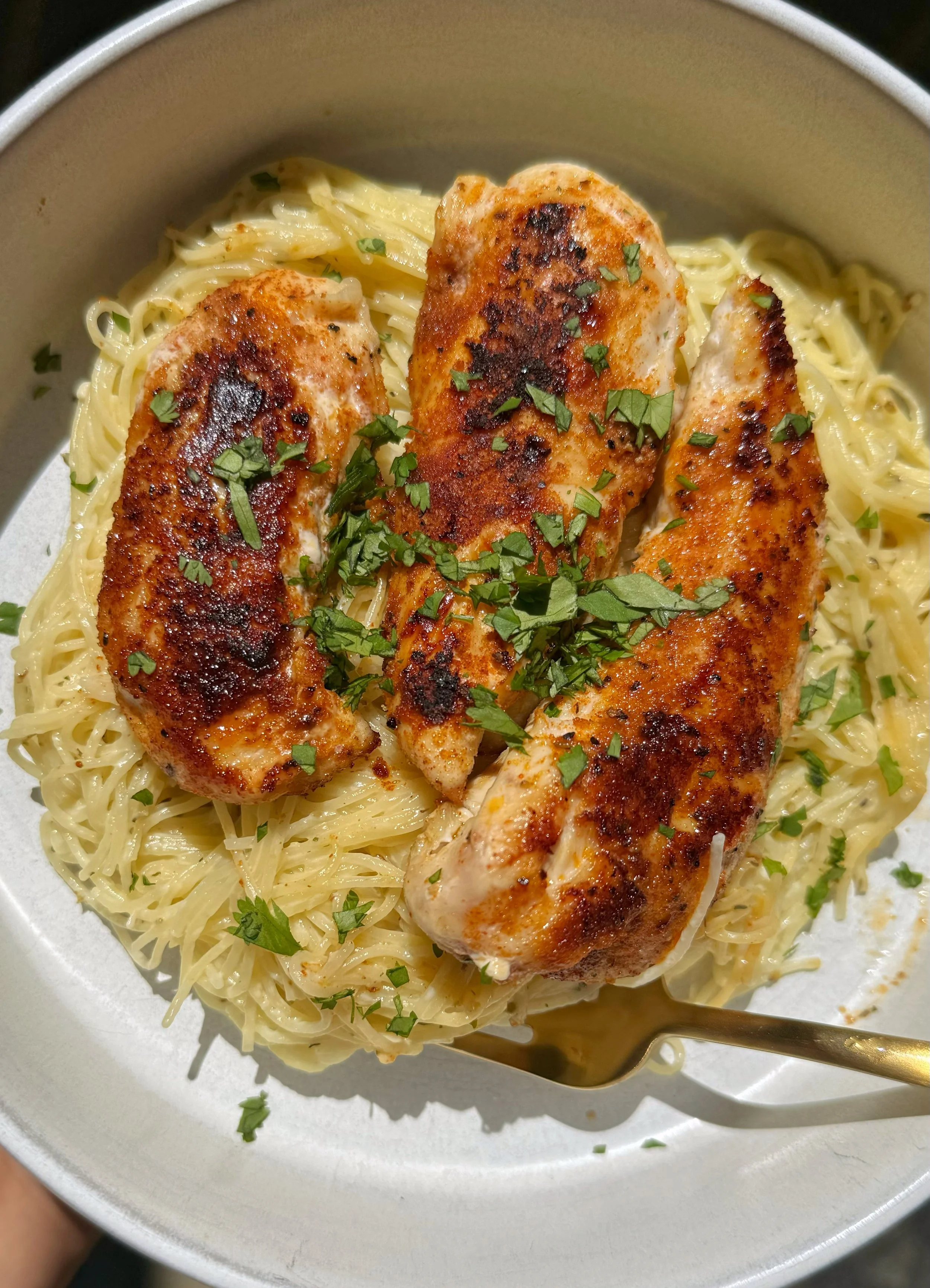 A bowl of crispy chicken on a bed of pasta with fresh basil on top.