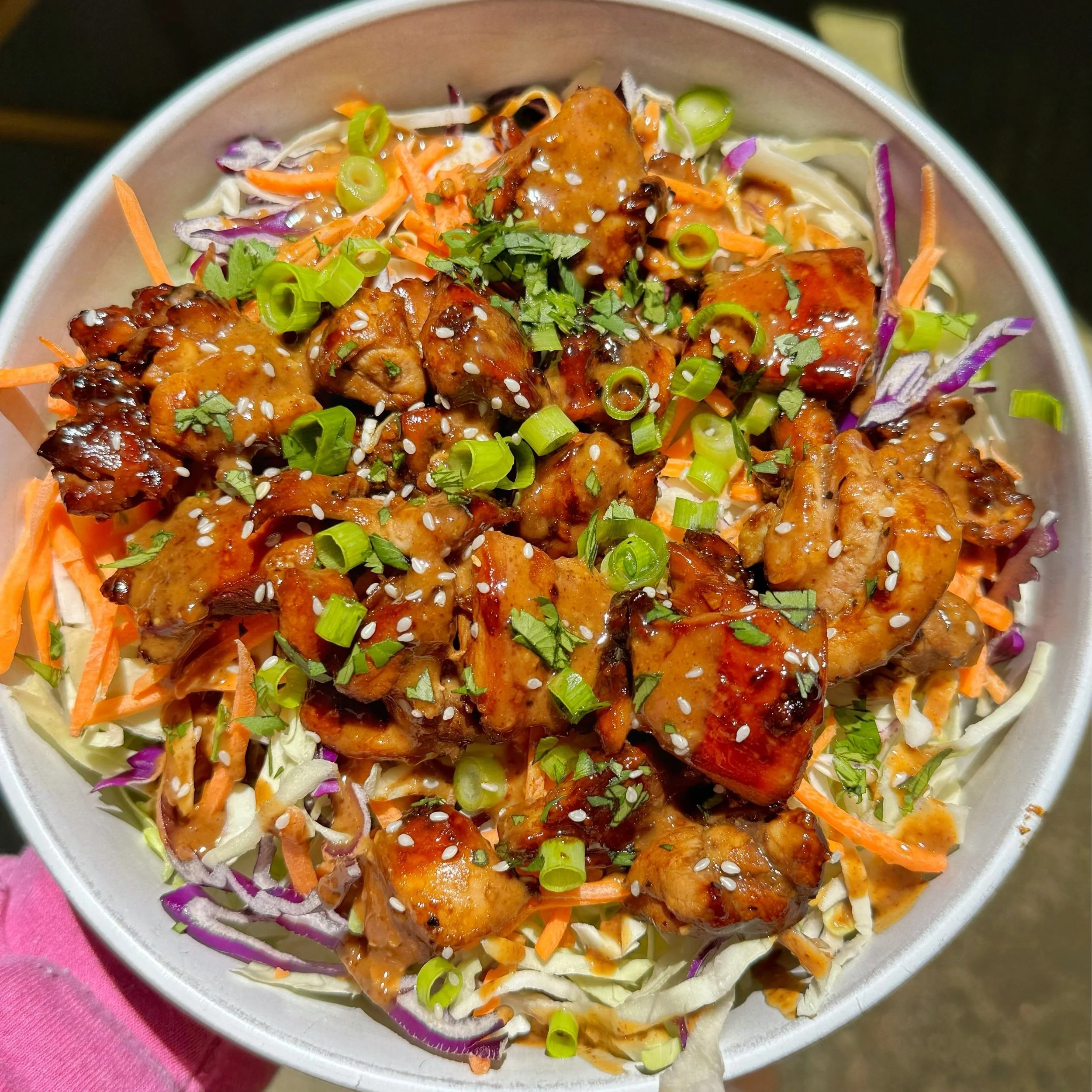 A bowl of sesame chicken on top of cabbage slaw mix garnished with chopped green onions and sesame seeds.