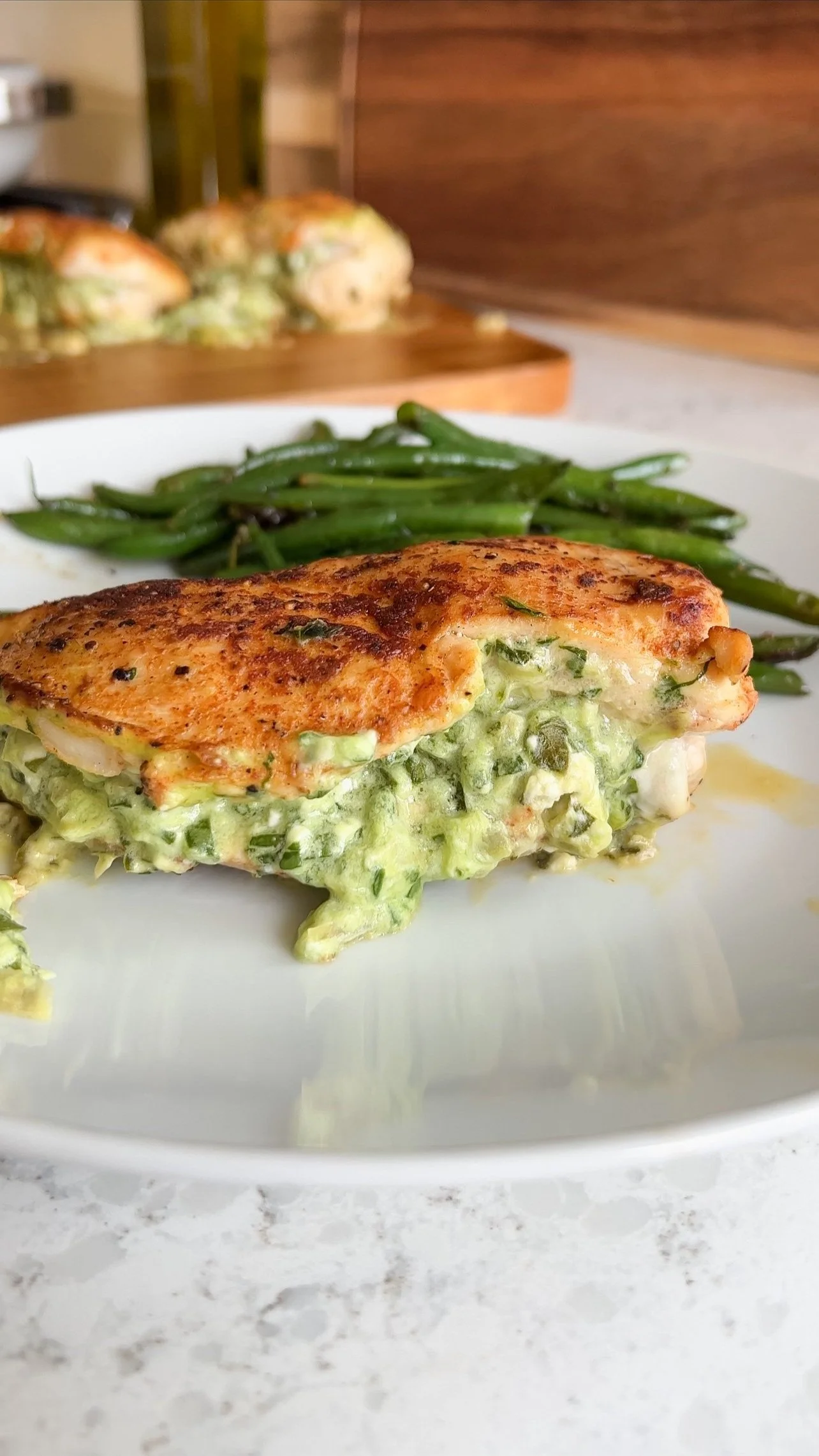 A plate of chicken breasts stuffed with spinach, artichokes and cheese with a side of green beans.