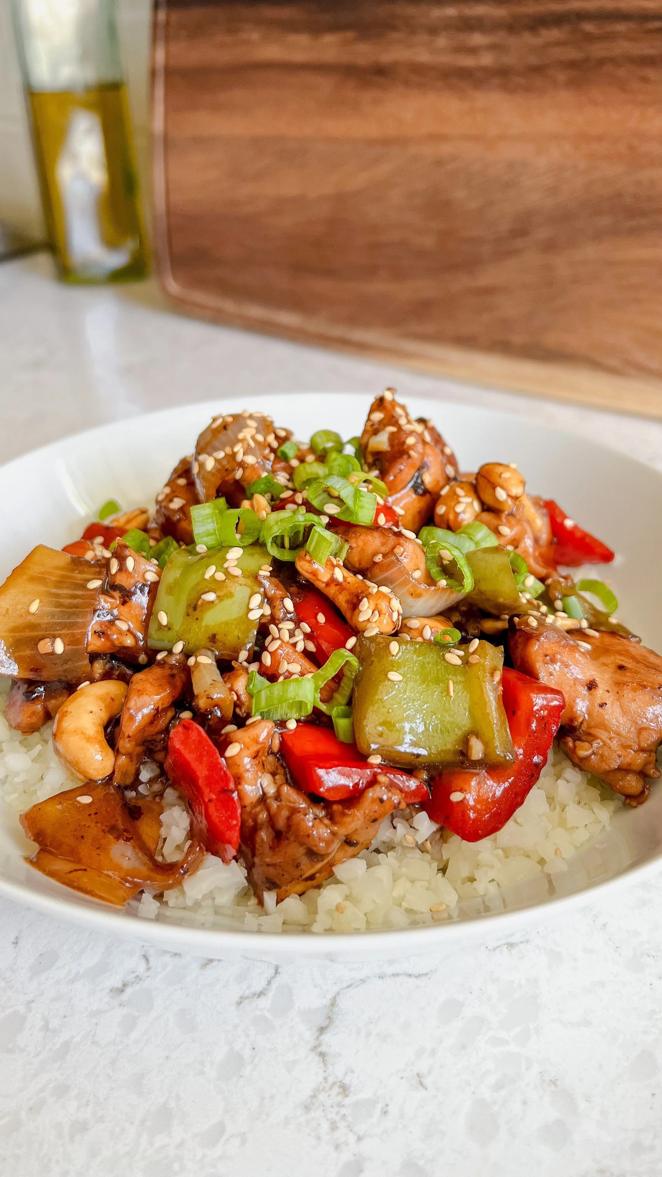 A bowl of chicken, cashews, bell peppers & onions on a bed of rice topped with green onions & sesame seeds.