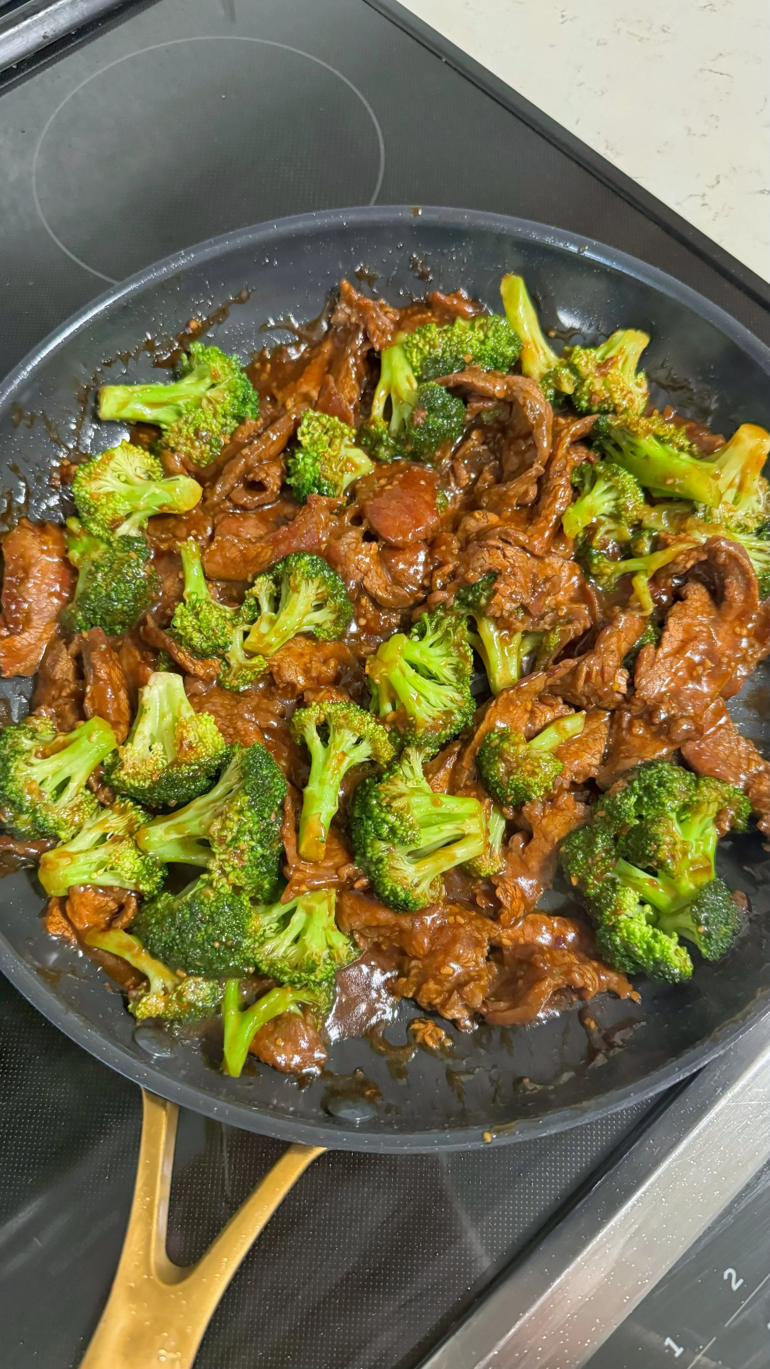 A frying pan with beef & broccoli in it with a glaze sauce mixed in it. 