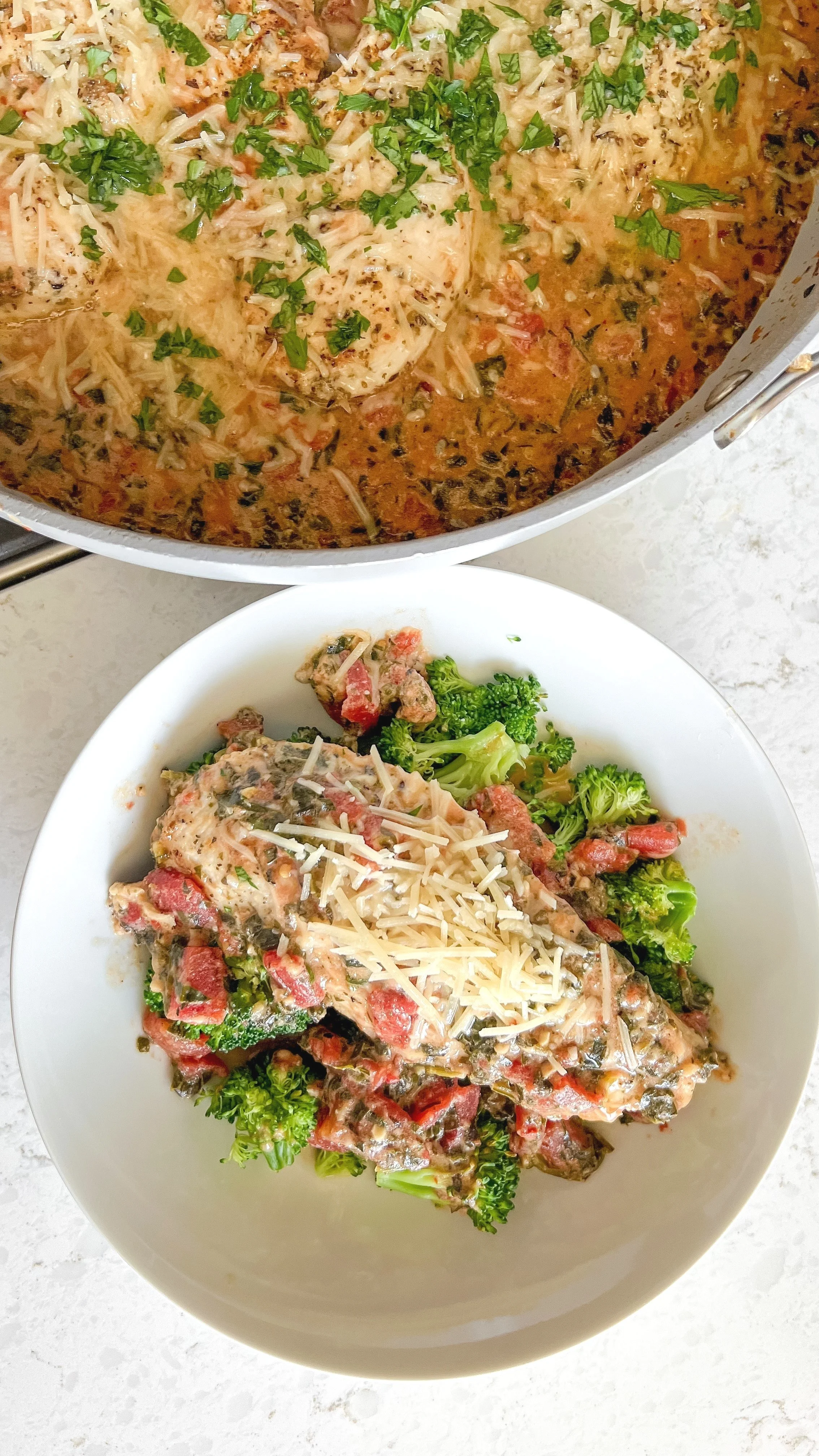 A bowl of broccoli, chicken, roasted tomatoes with parmesan cheese on top sitting next to a pan of the Italian chicken.