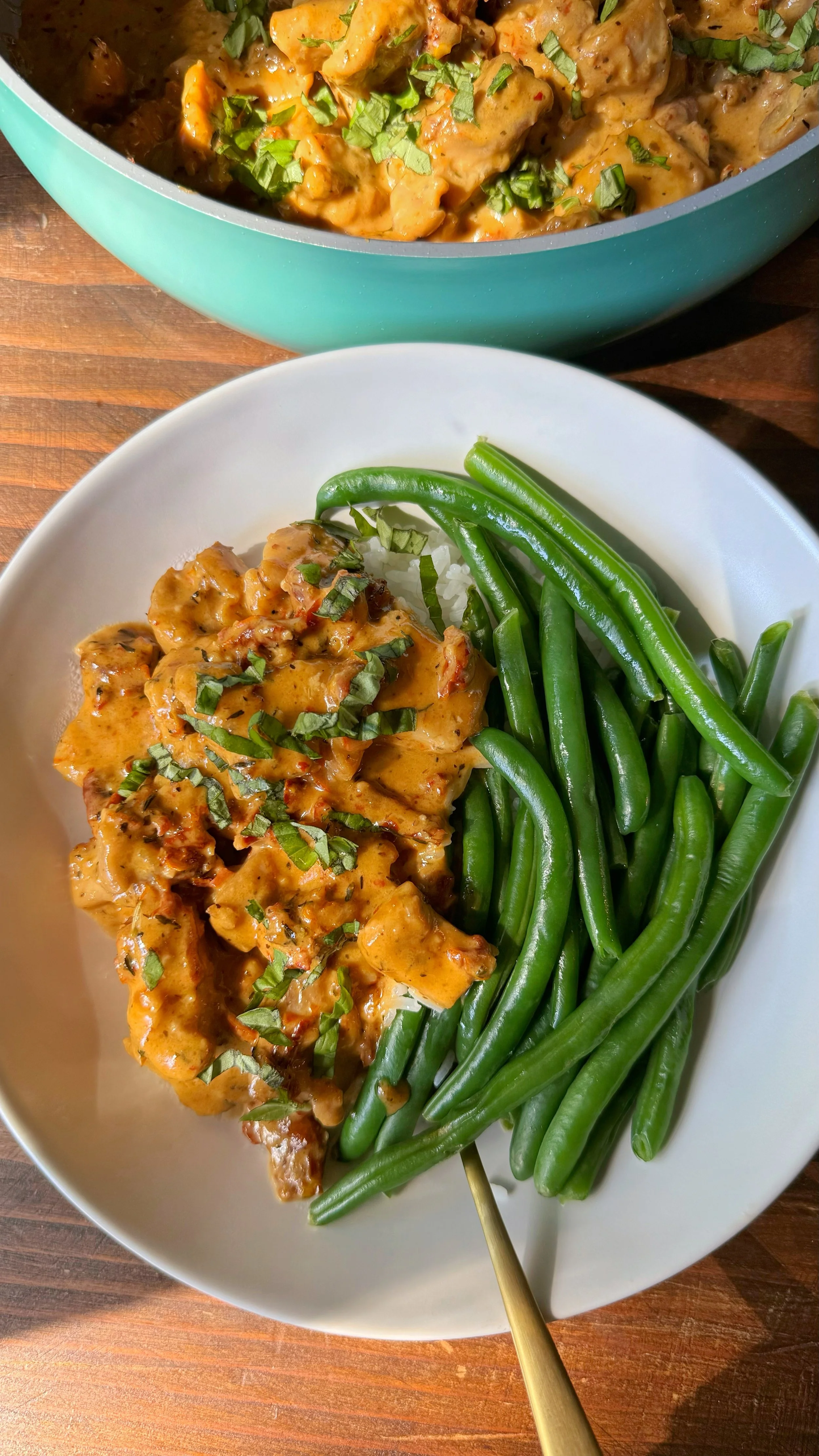 A bowl of chicken with a glaze like sauce served over rice with chopped fresh basil on top and a side of green beans. 