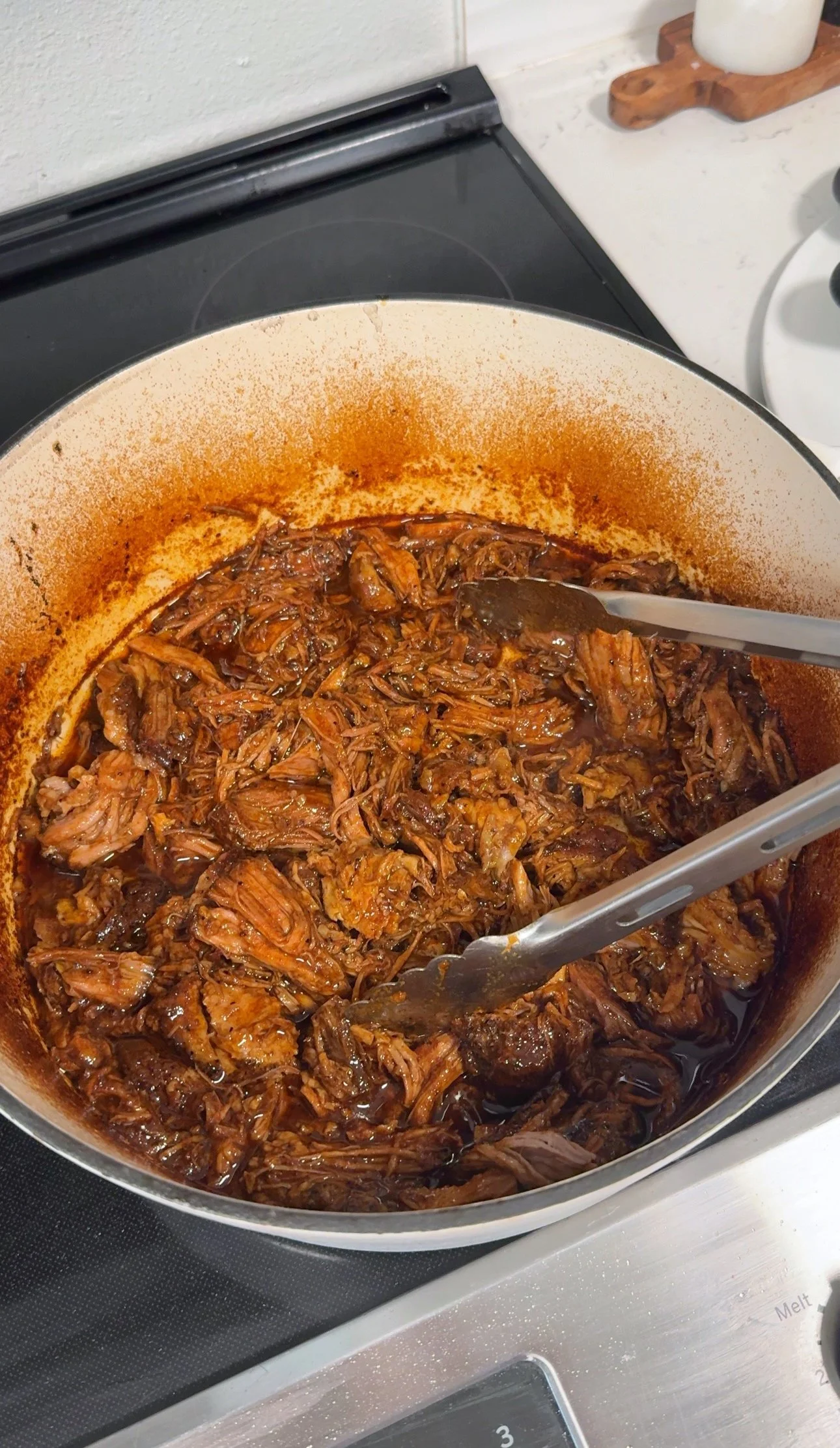 A pot of BBQ shredded pork with tongs inside the pan.