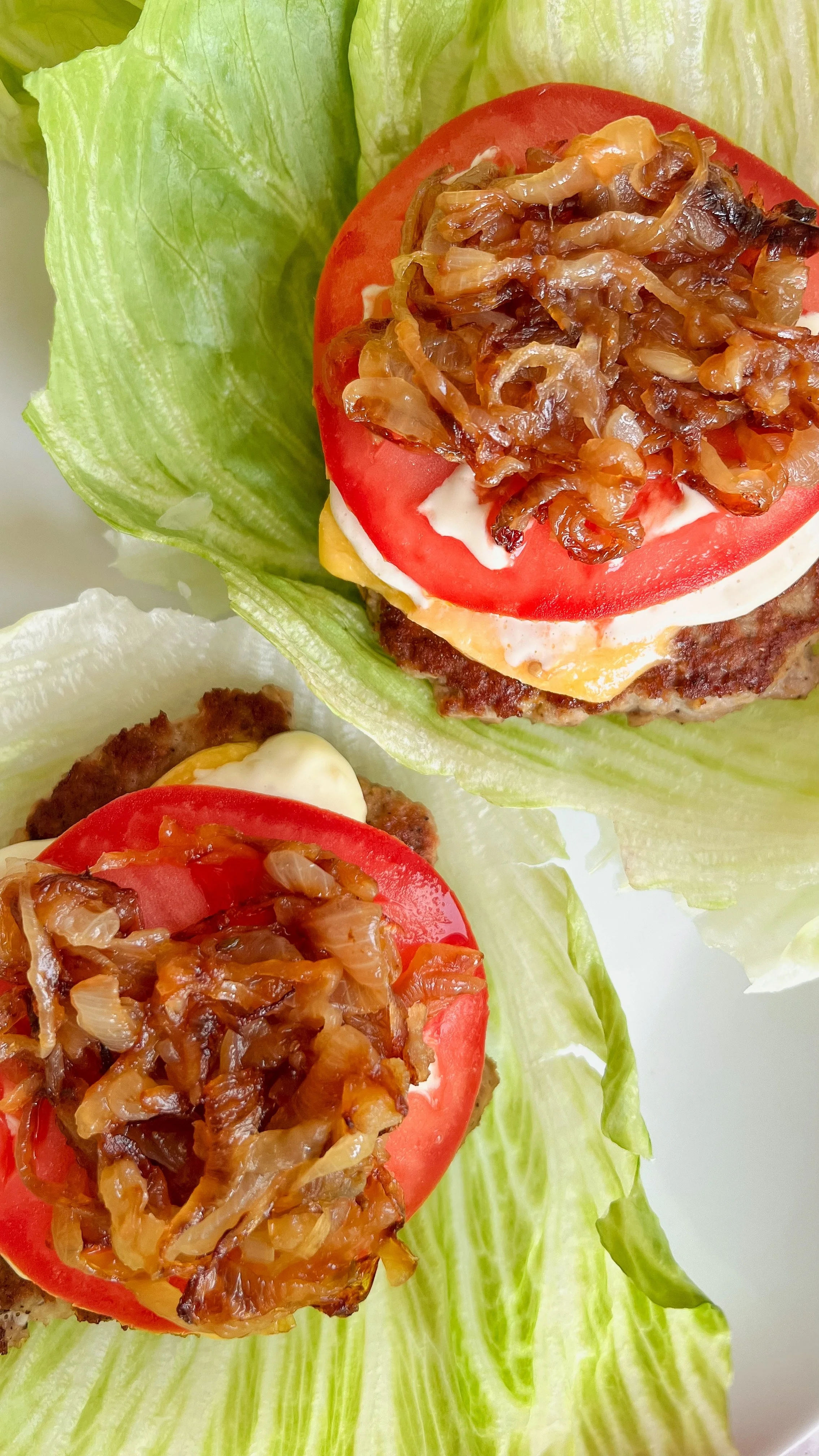 A turkey burger with tomato, Aioli sauce, cheese, caramelized onions and bacon on top laying on a bed of lettuce.