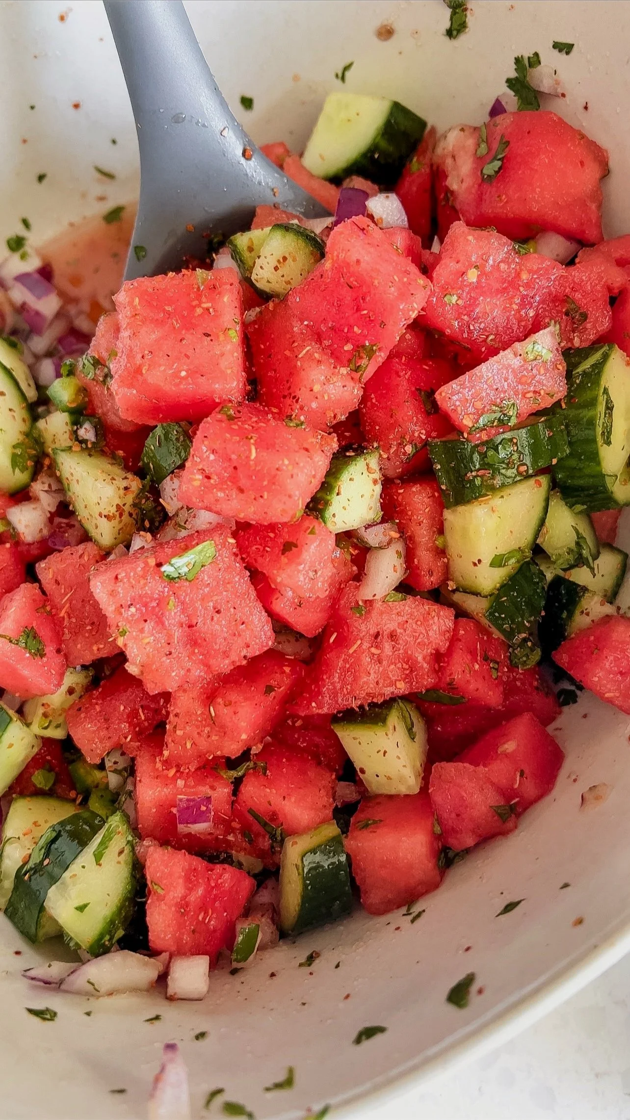 A close up shot of a bowl of watermelon & cucumbers with chopped red onions, Tajin and fresh cilantro.