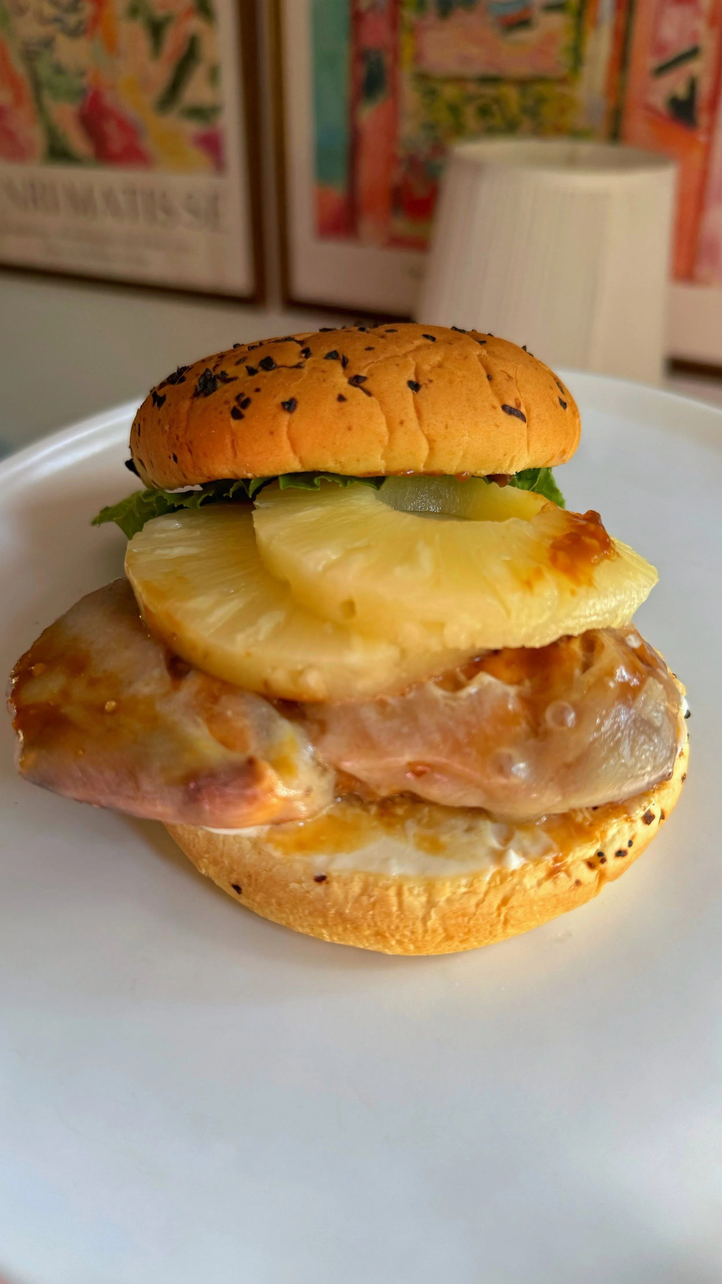 A close up shot of a chicken burger with pineapple slices, lettuce and a sauce inside of a bun.