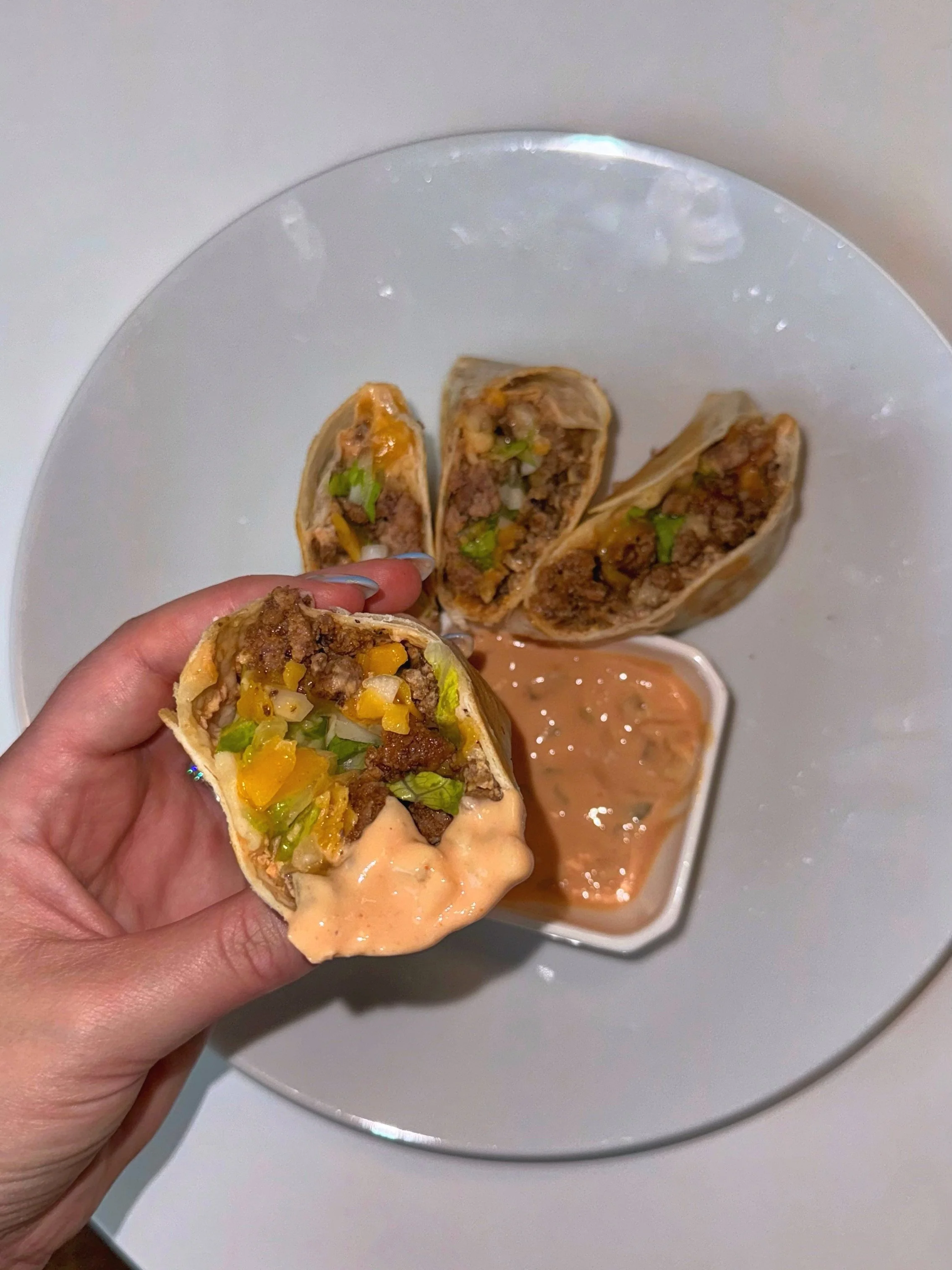 Ground beef, lettuce, onion, cheese inside of a tortilla and rolled to look like a taco with a small bowl of goop sauce on the side.