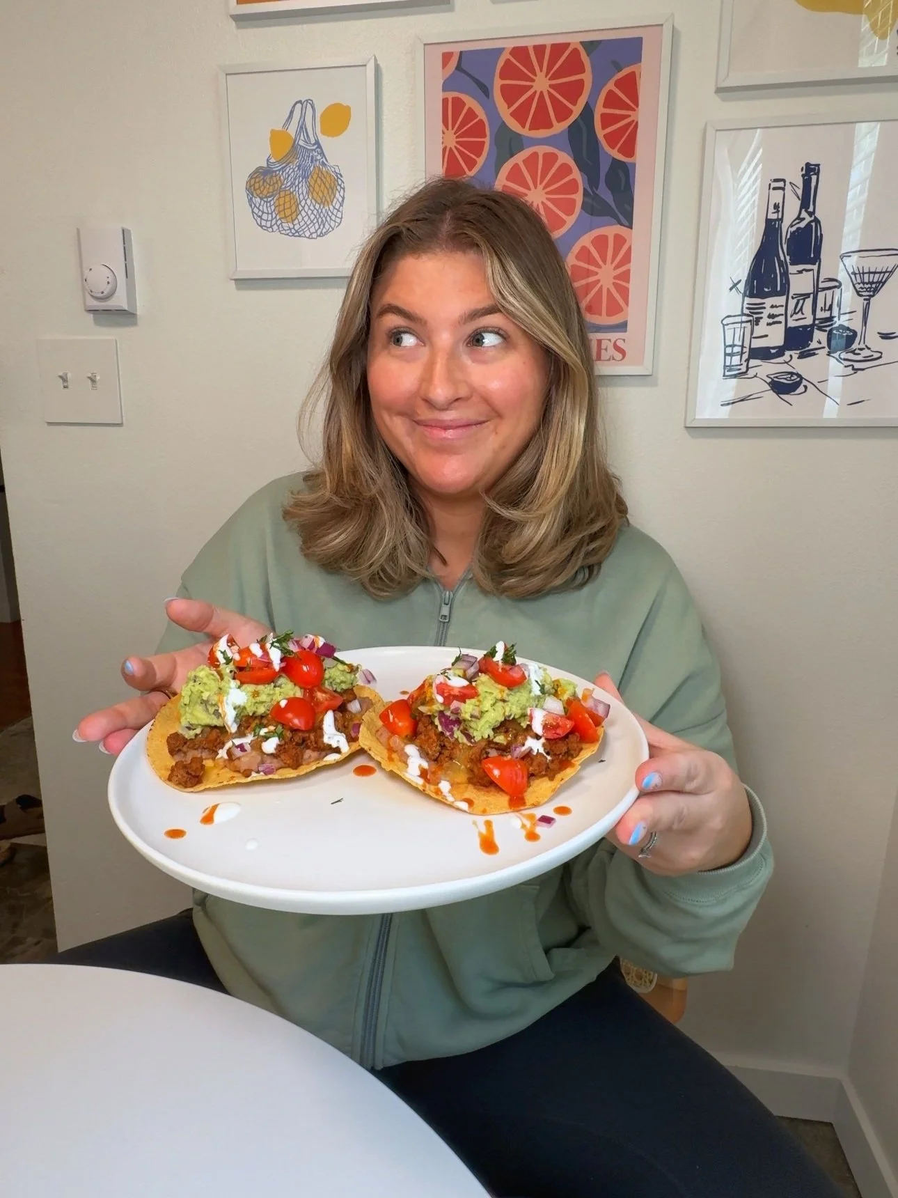A plate being held with two tostadas filled with ground turkey, avocado, tomato, chopped red onion and cilantro with a drizzle of hot sauce.