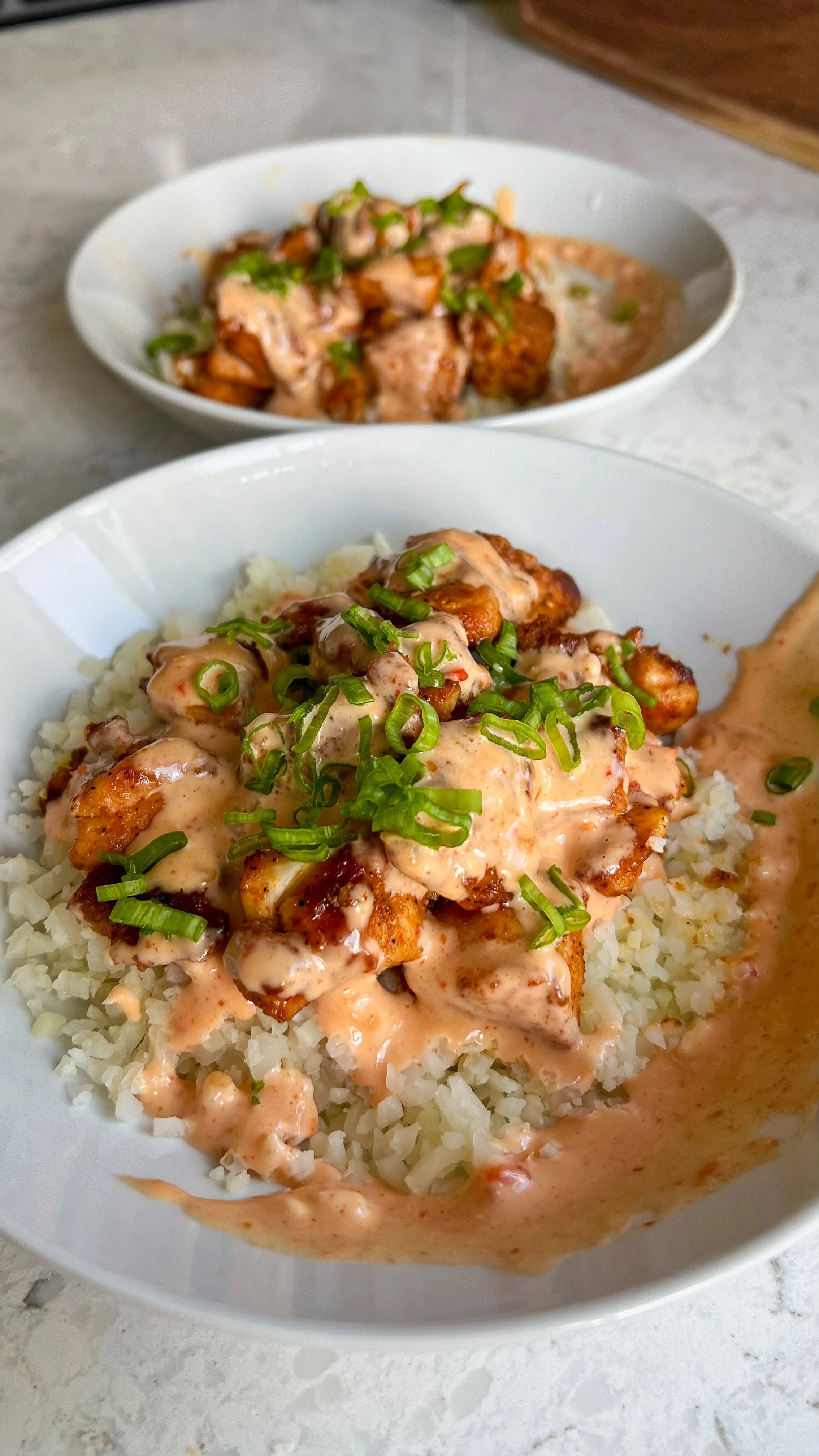 Two bowls of crispy chicken on a bed of cauliflower rice topped with green onions and a dressing.