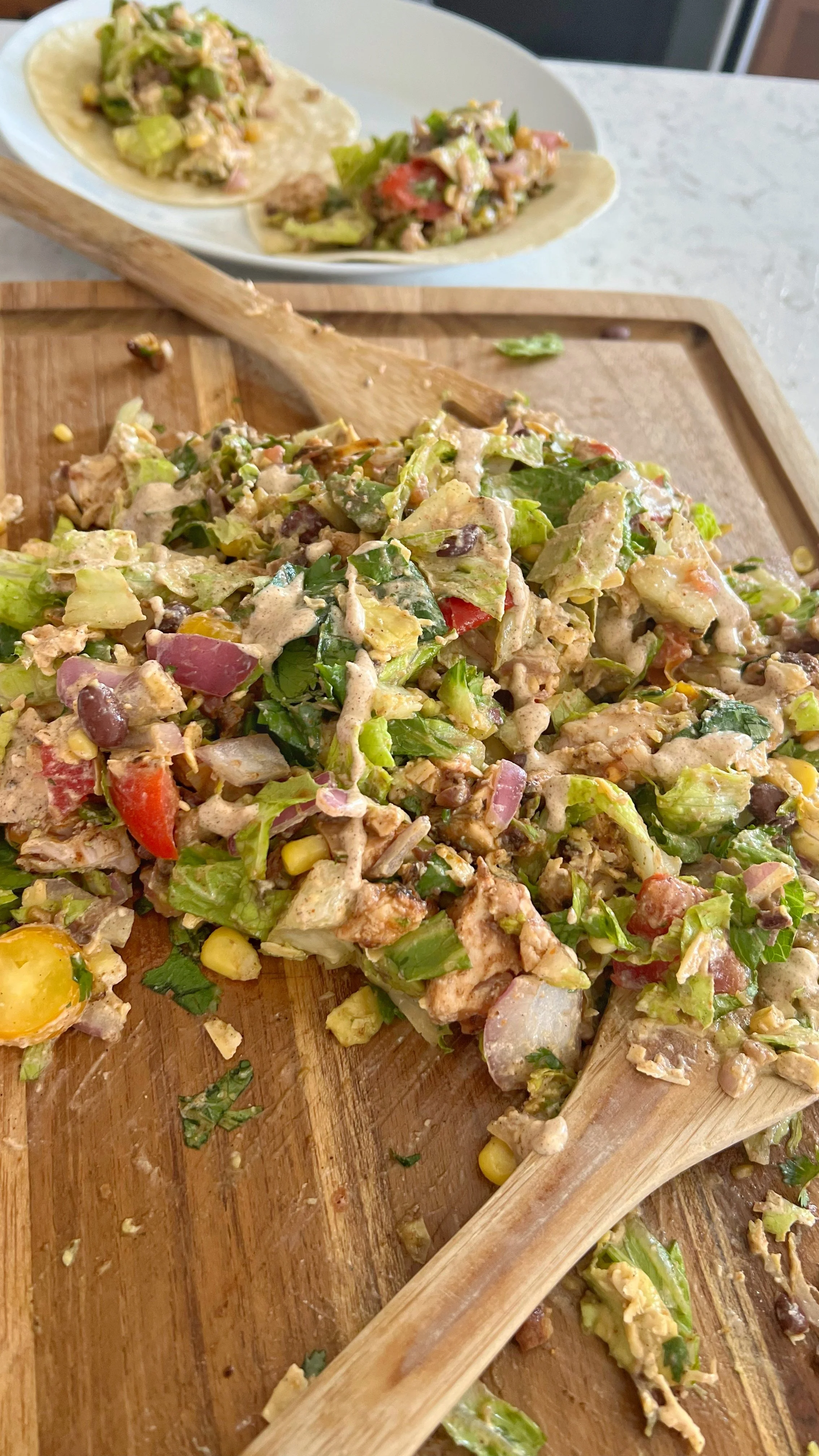A close up shot of a chopped salad with lettuce, red onion, black beans with a dressing on top of a cutting board.