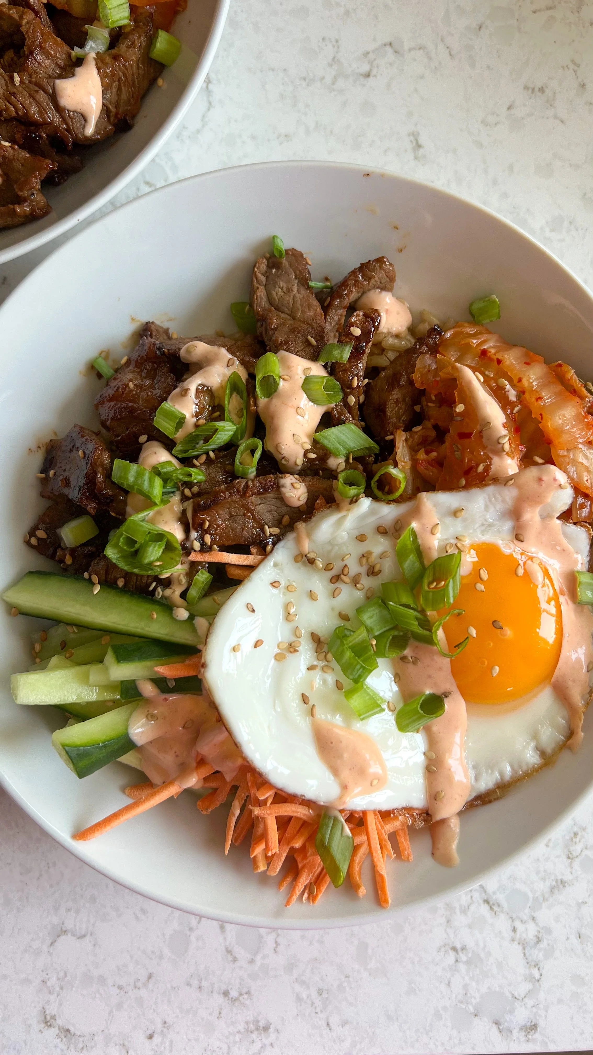 A bowl of beef, shredded carrots, onions with a egg, chopped green onions and a dressing on top 