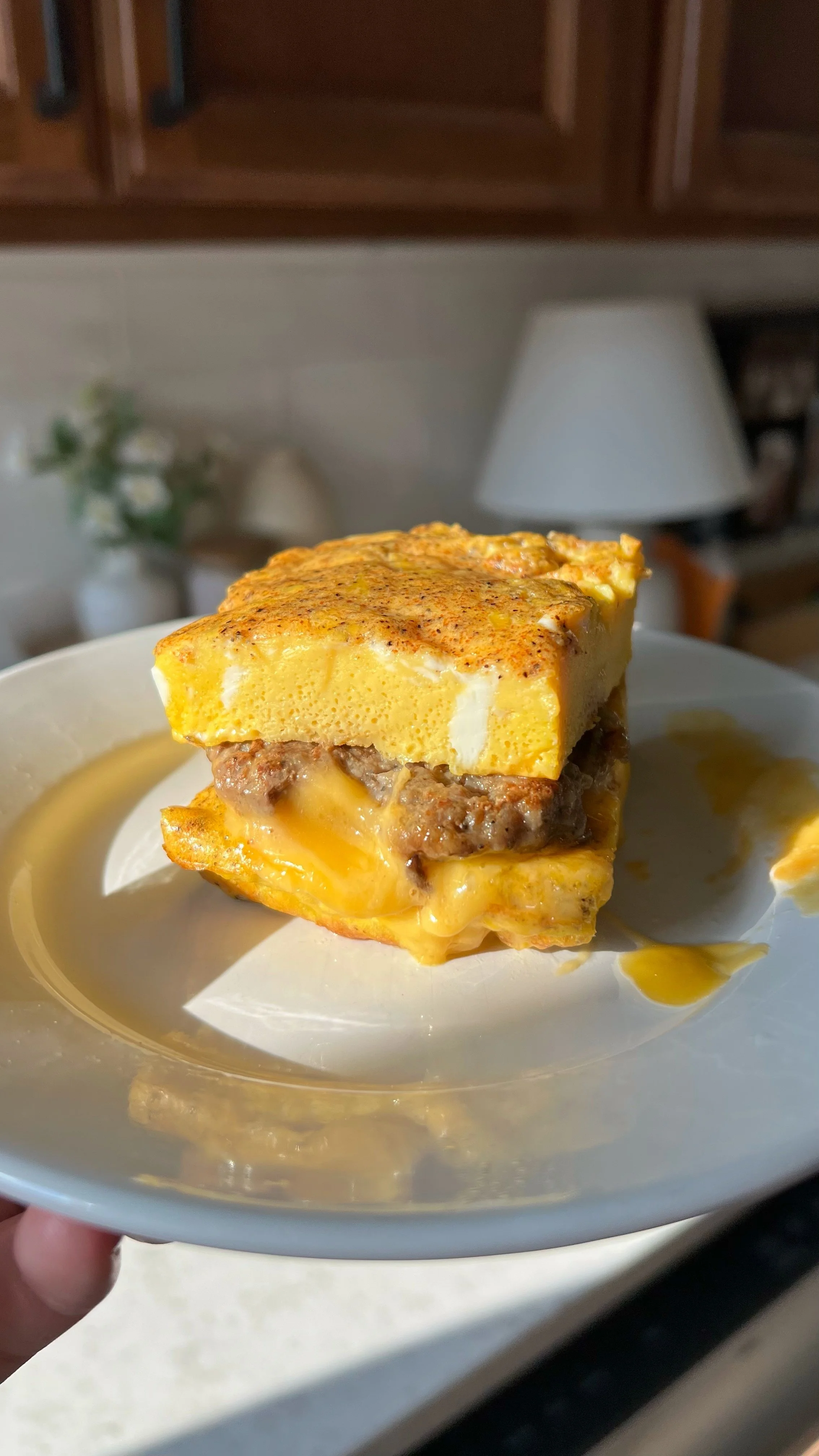 An egg sandwich with sausage and cheese inside sitting on a plate.