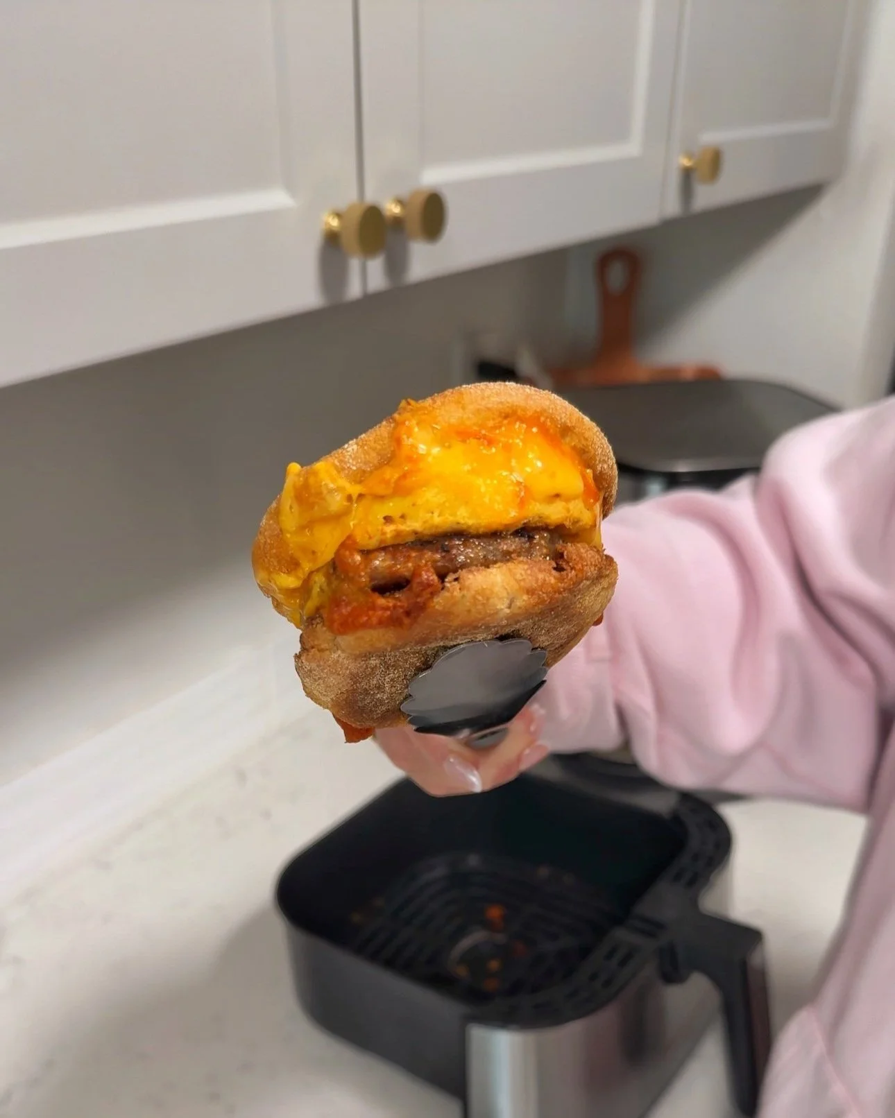 A sausage egg & cheese breakfast sandwich being held up with tongs.