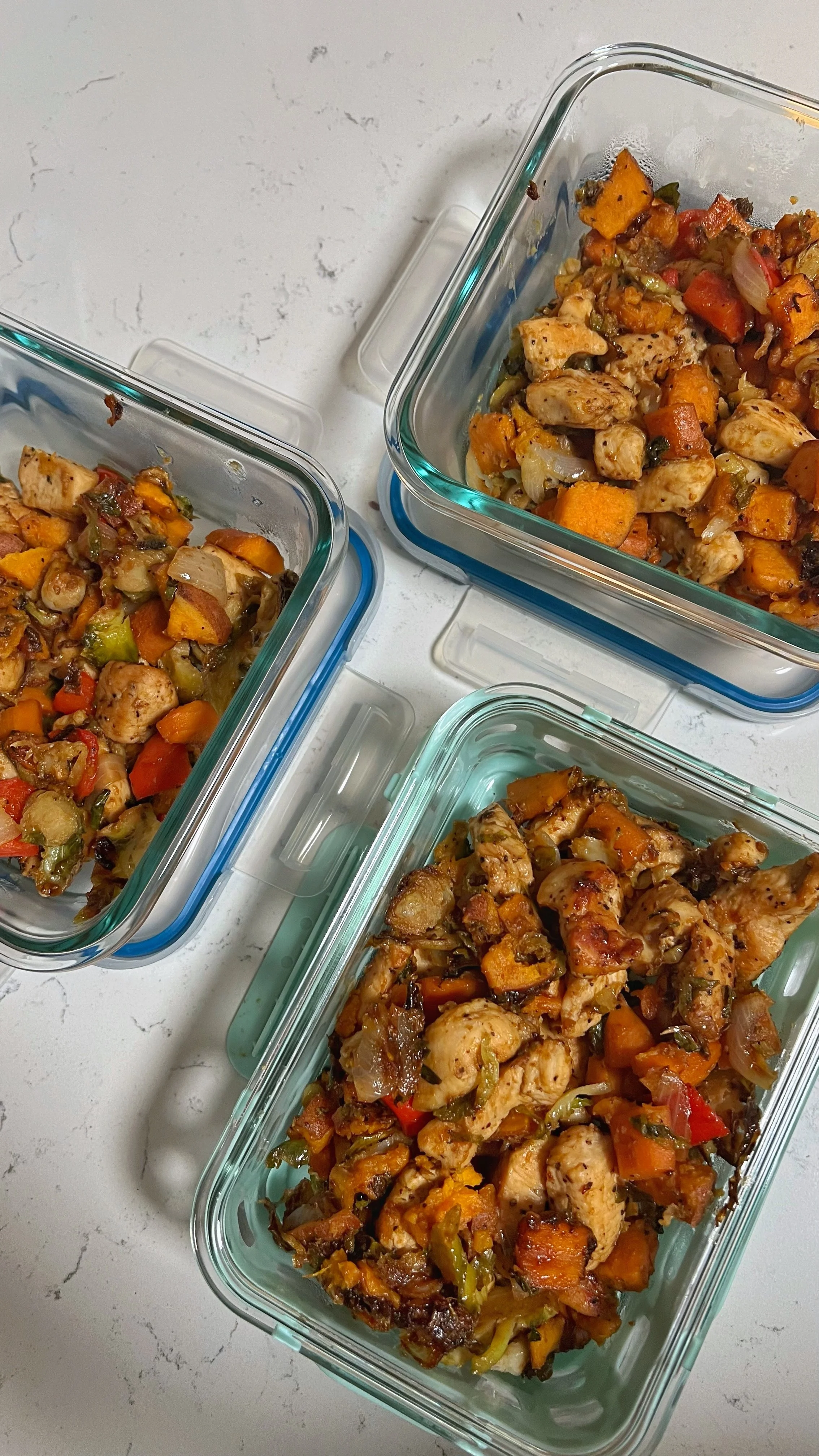 Chicken chunks, cooked carrots, peppers and Brussels sprouts with a glaze on top added to food storage containers.