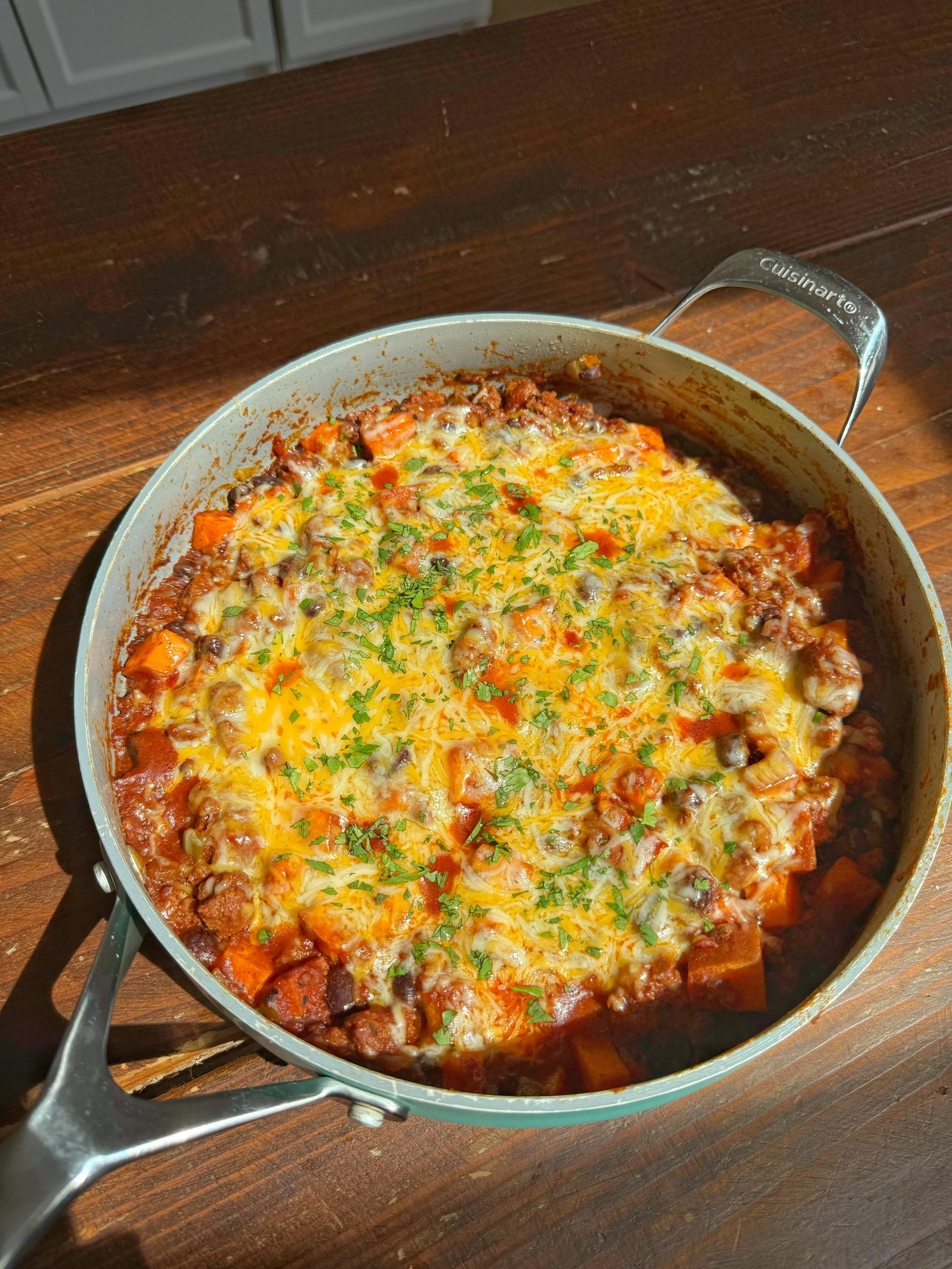 A pan of sweet potato, black beans, crushed tomatoes topped with melted cheese and fresh cilantro.