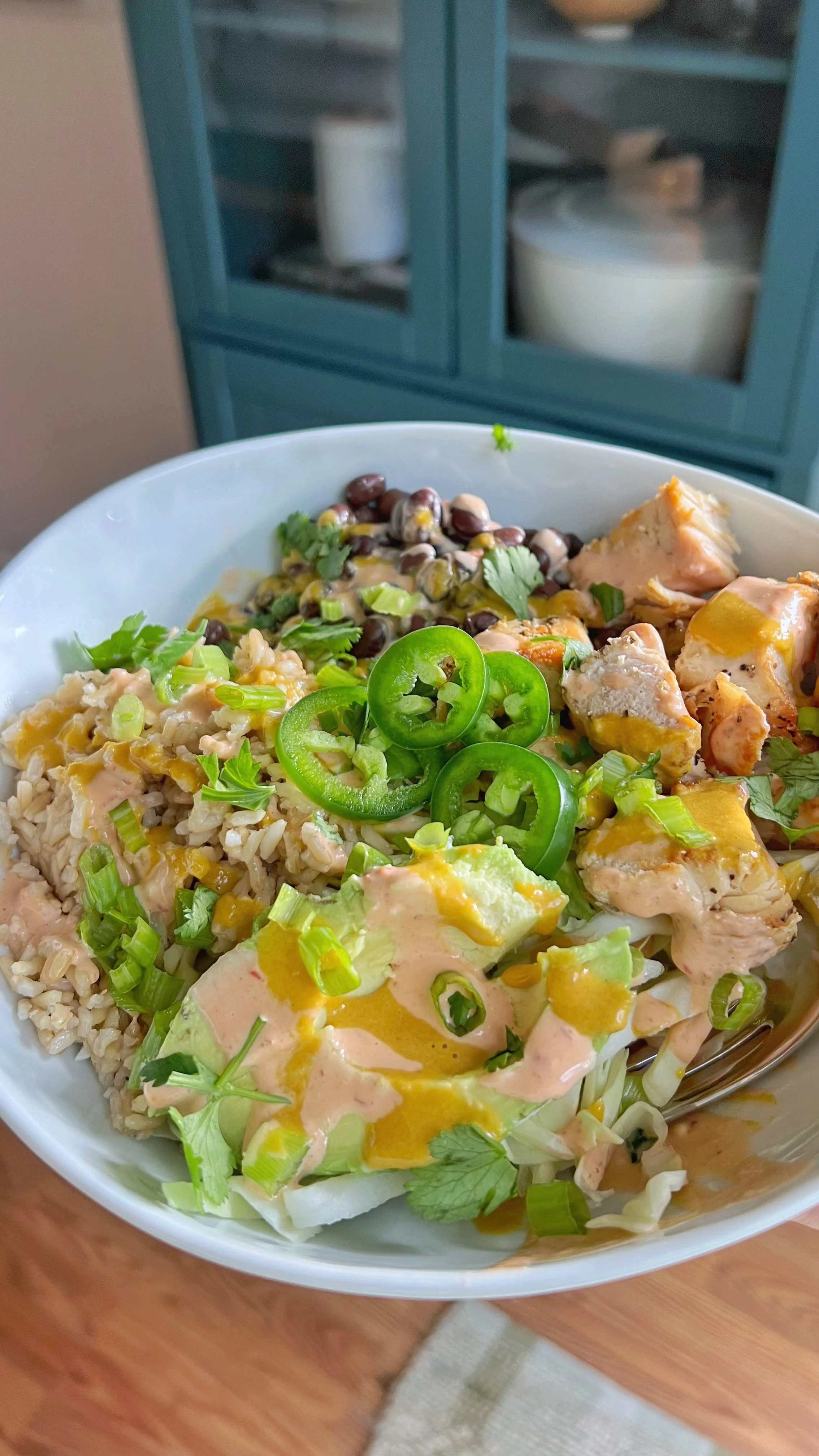 A bowl of chicken, black beans, cilantro, jalapeños with a dressing on top, all on a bed of brown rice. 