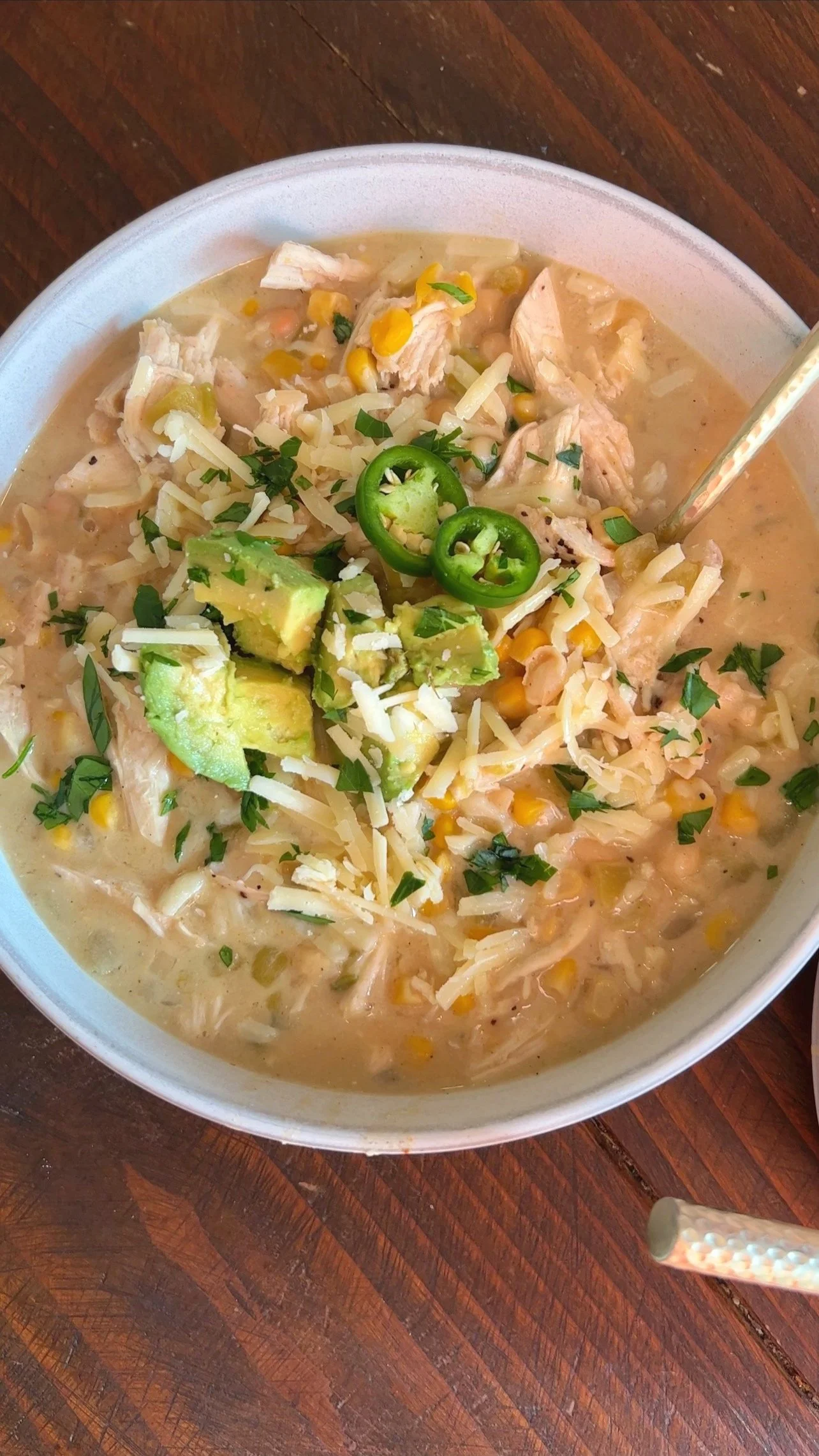A bowl of white chicken chili with avocado, cilantro and Jalapeños on top.