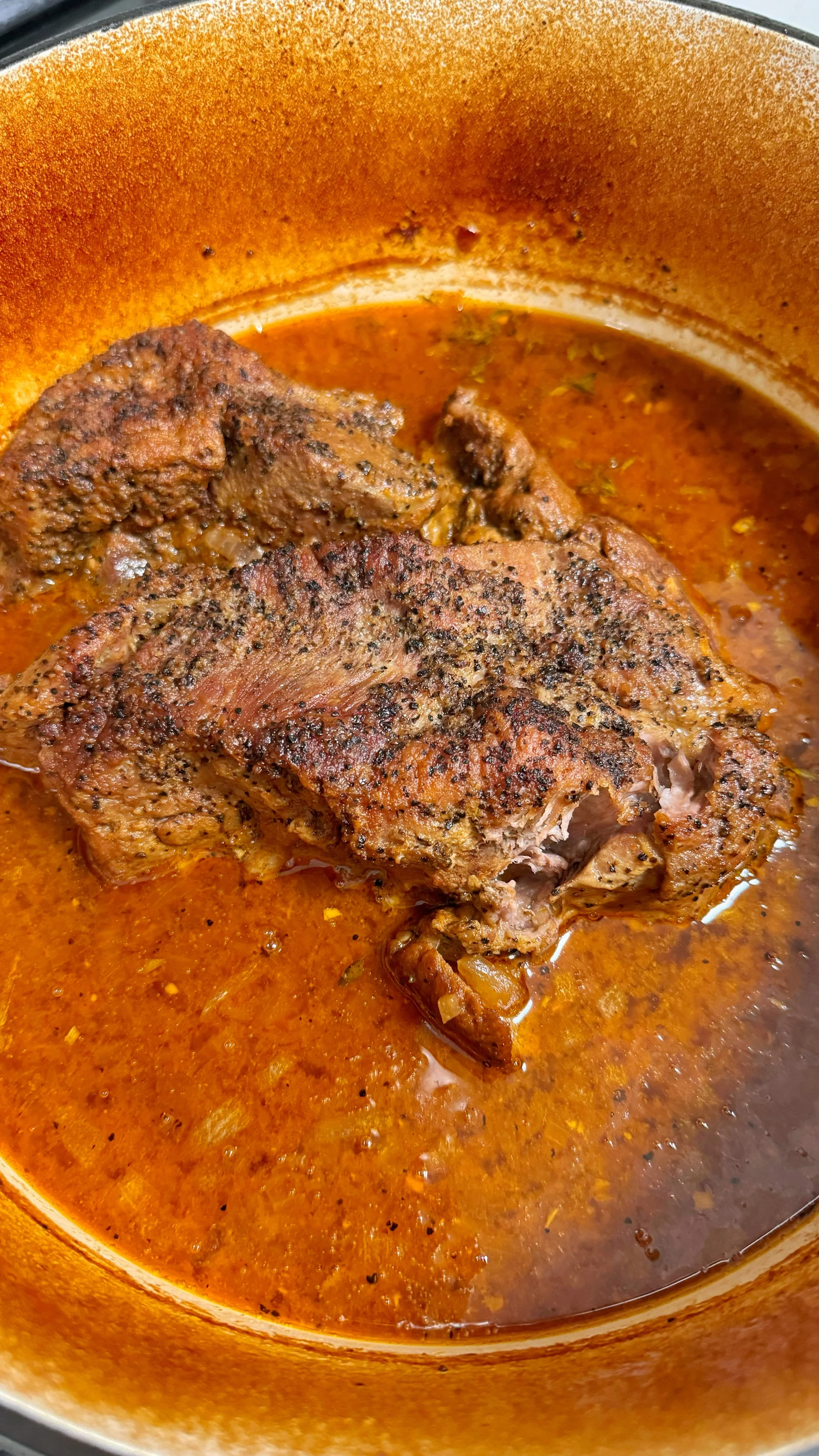 A pot of pork butt with seasonings in sauce.