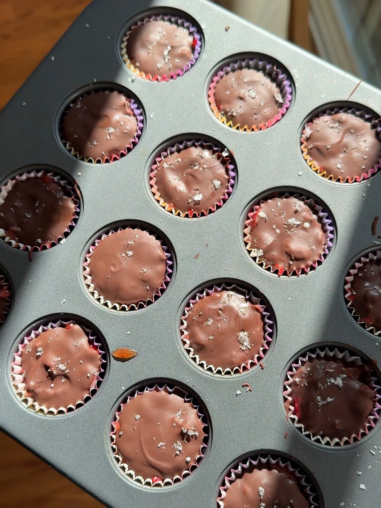 A muffin tin that is full of chocolate cups that have flake salt on top.