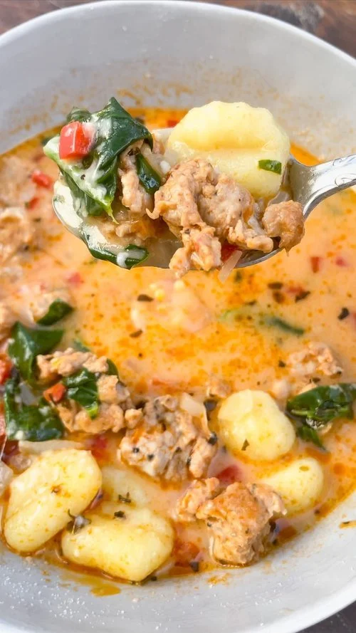 A close up shot of sausage & gnocchi soup with grated parmesan cheese on top.