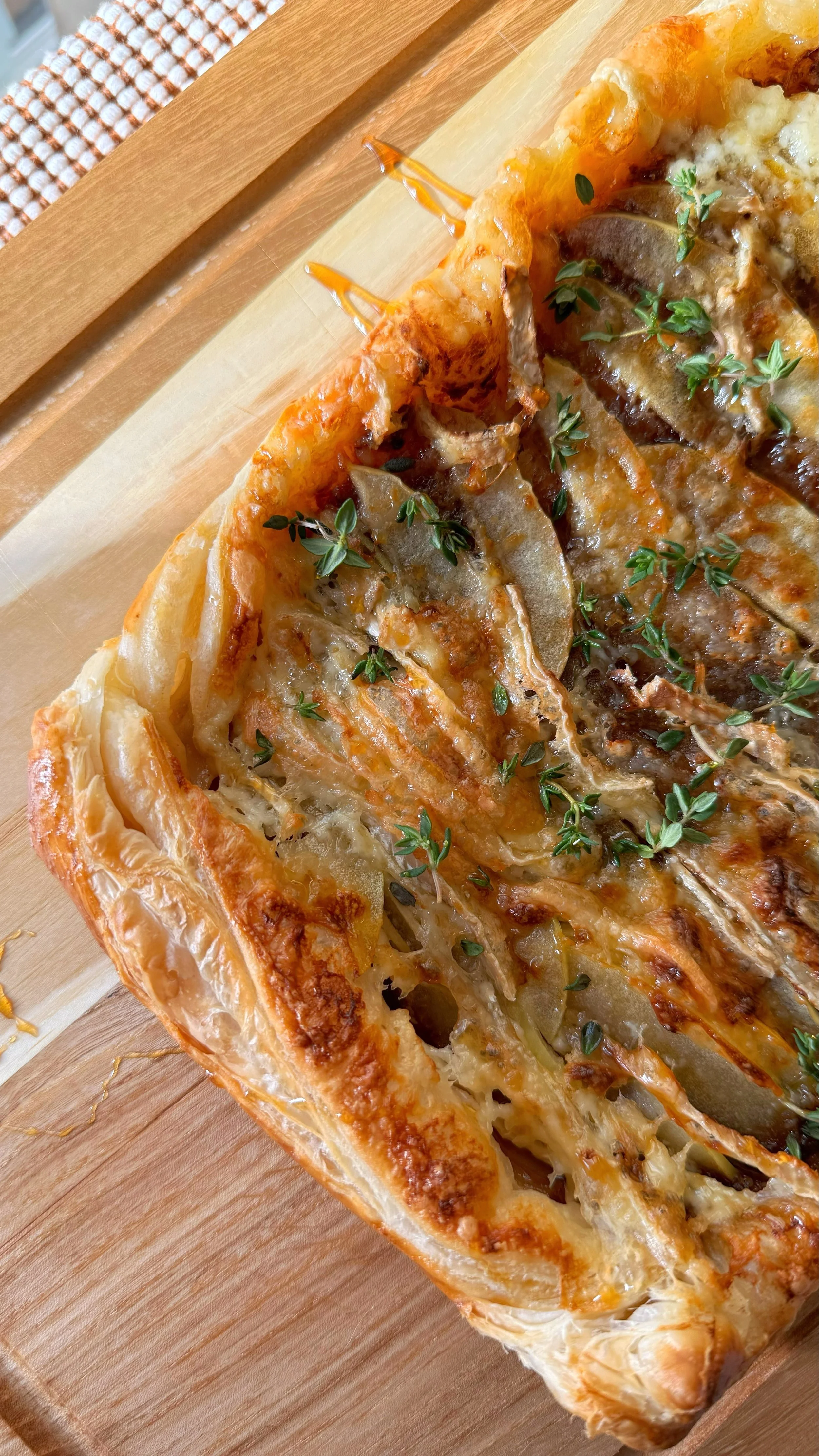 An apple brie tart pastry on top of a cutting board topped with fresh thyme and drizzle of honey.