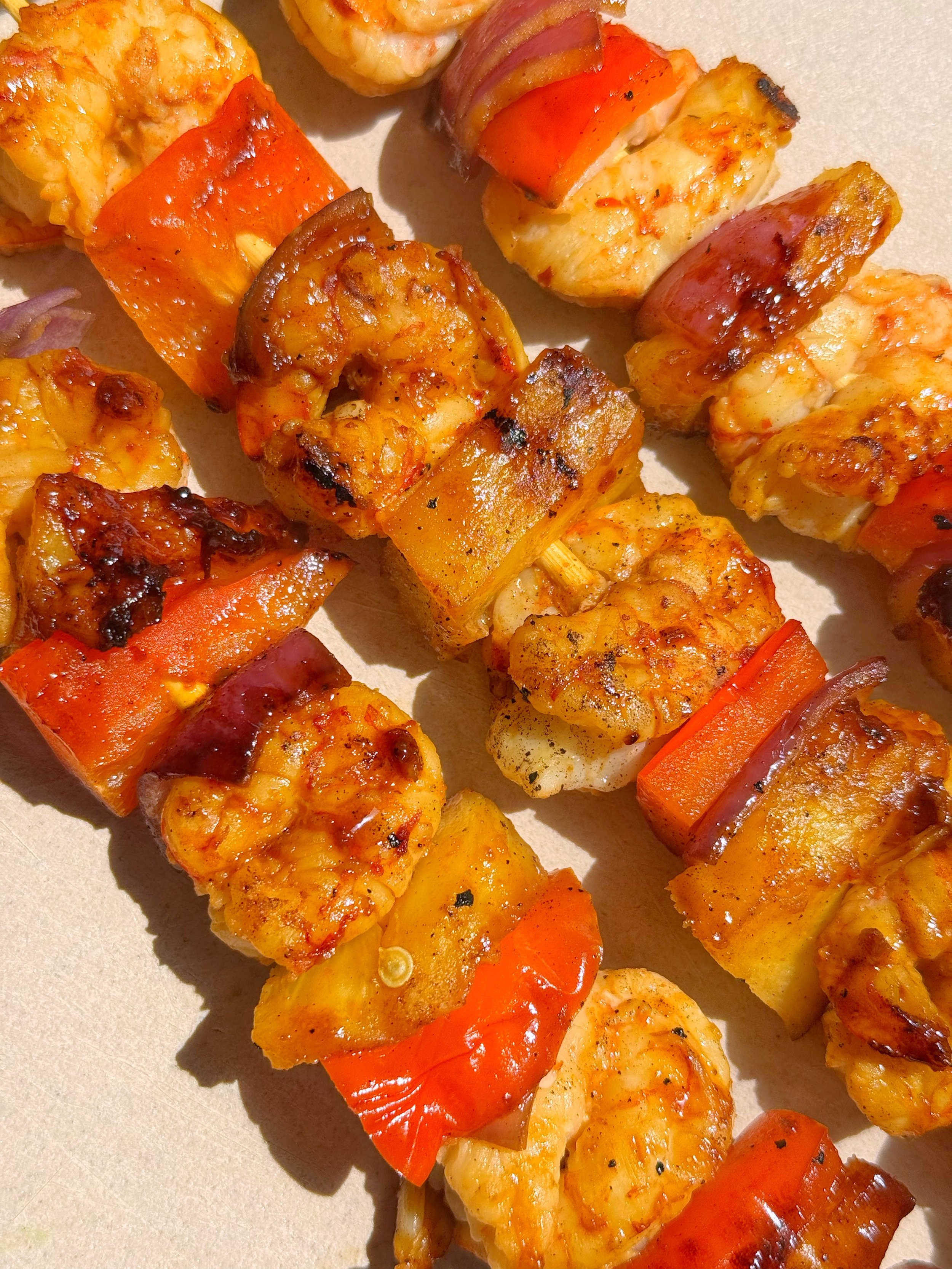 Skewers that have shrimp, pineapple, red pepper, and red onion with a glaze on them.